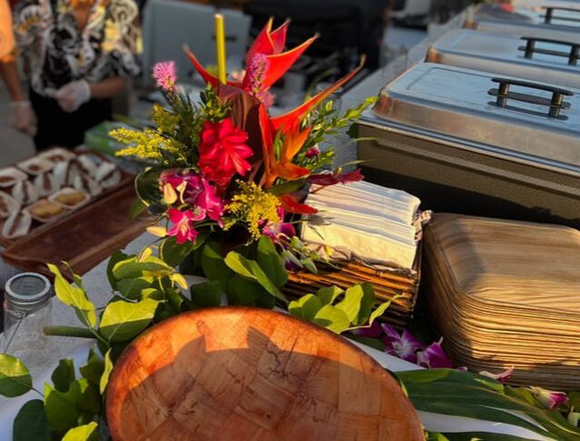 Hawaiian authentic catering set up, with chaffing dishes, bamboo plates, napkins, cutlery, and wooden bowls for delicious Hawaiian-style food. Tropical floral centerpiece and fresh greenery to add a flair of island decor.