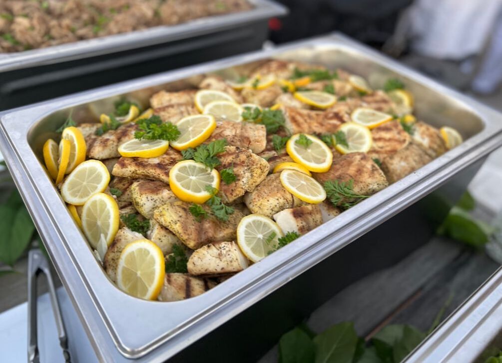 A coconut salmon and lemon dish, served with green onions, in a silver chafing dish at a Hawaiian themed and authentic luau in southern california.