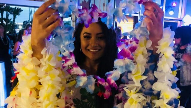 A beautiful lei greeter wearing an array of faux silk leis in many vibrant colors, offering a warm and welcoming presence.